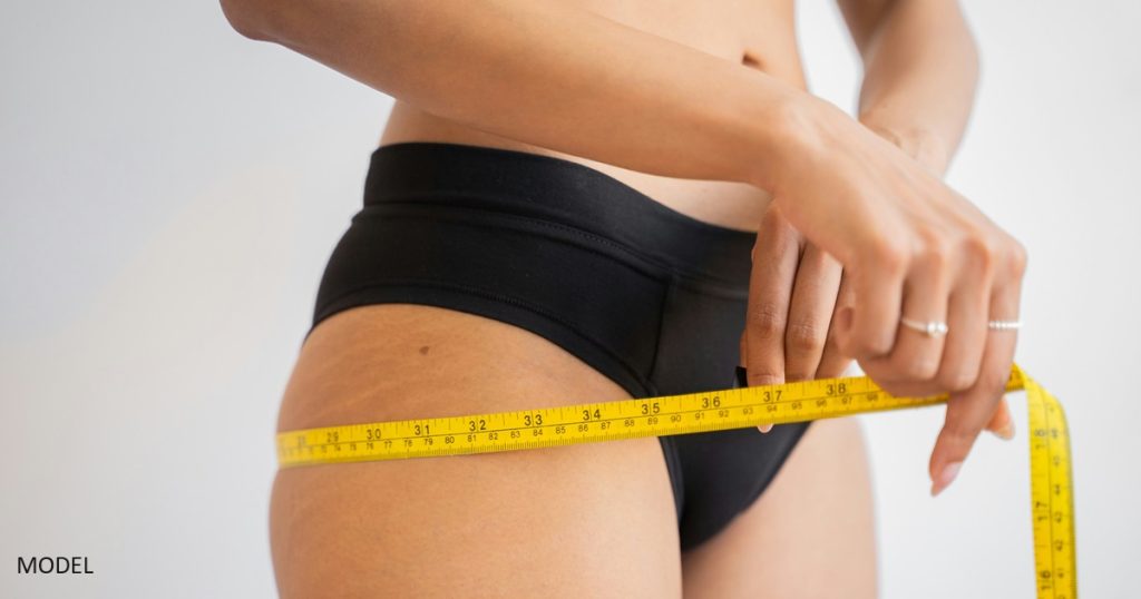 Woman using measuring tape on her hips